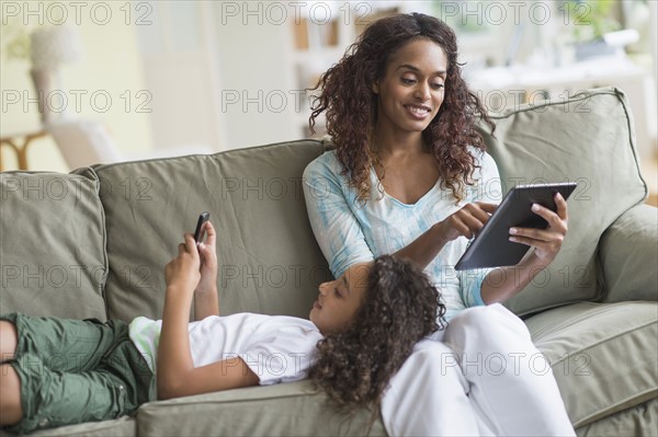 Mother and daughter (8-9) relaxing on sofa.