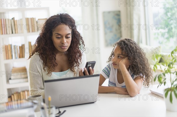 Mother and daughter (8-9) using laptop and smart phone.