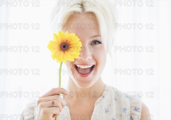 Portrait of blonde woman holding yellow flower.