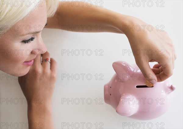 Woman putting coin into piggy bank.