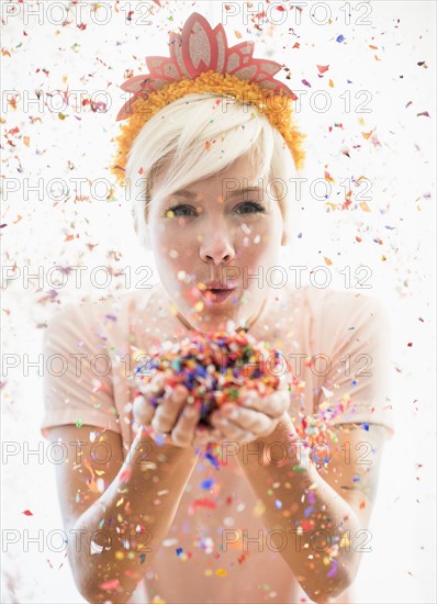 Woman wearing tiara blowing confetti.