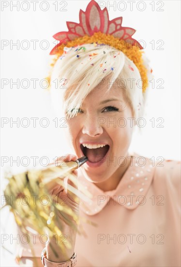 Woman wearing tiara blowing party horn blower.