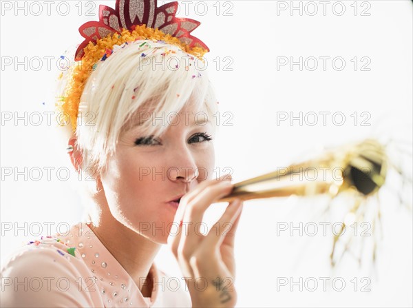 Woman wearing tiara blowing party horn blower.