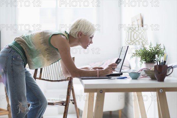 Woman using laptop and cell phone at home.