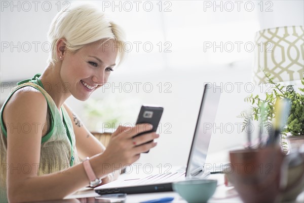 Woman using cell phone and laptop at home.