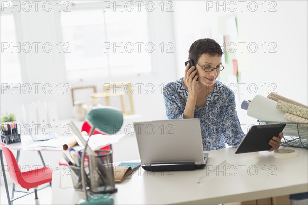 Senior business woman using cell phone and tablet pc in office.