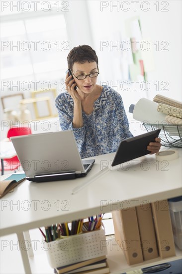 Senior business woman using cell phone and tablet pc in office.