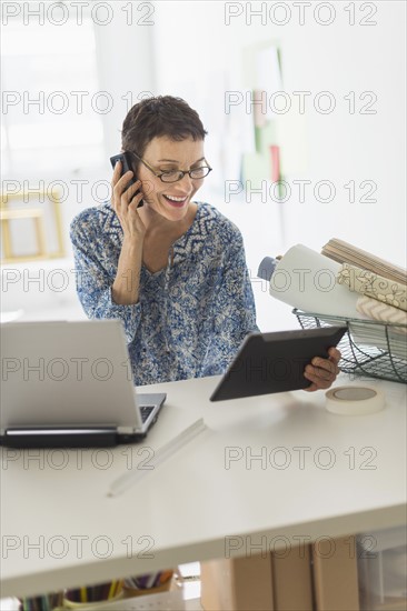 Senior business woman using cell phone and tablet pc in office.