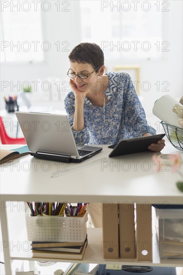 Senior business woman using cell phone and tablet pc in office.