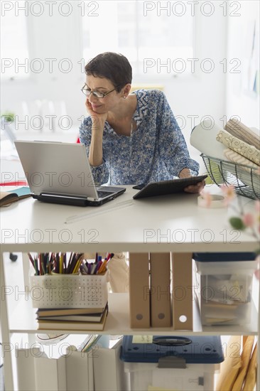 Senior business woman using cell phone and tablet pc in office.