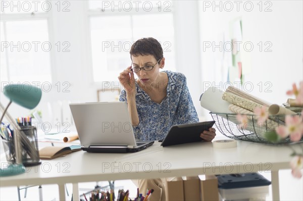 Senior business woman using laptop and tablet in office.