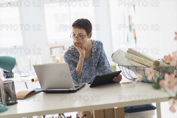 Senior business woman using laptop and tablet in office.