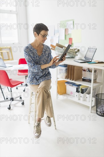 Senior business woman using laptop and tablet in office.