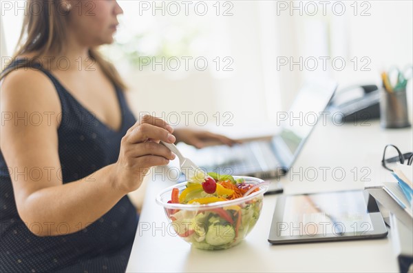 Woman working in home office and eating salad.