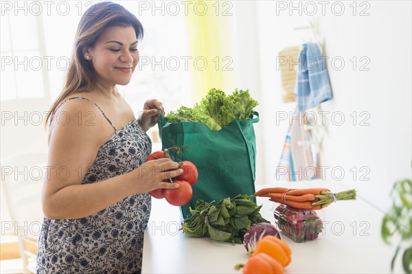 Woman taking out vegetables of grocery bag.