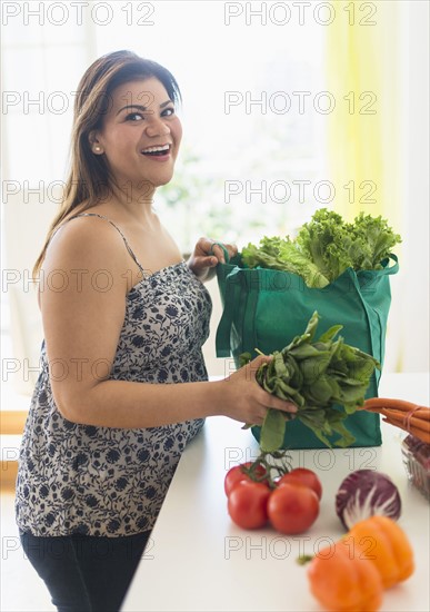 Woman taking out vegetables of grocery bag.