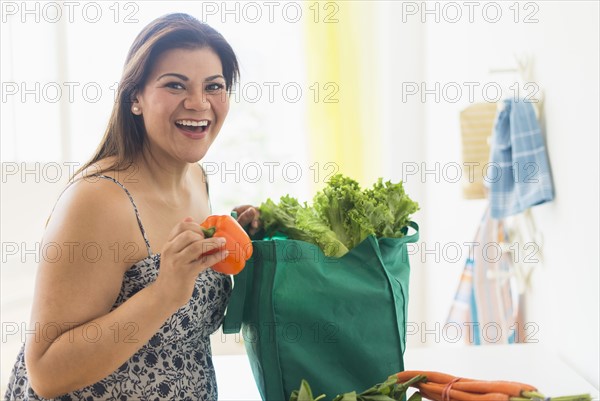 Woman taking out vegetables of grocery bag.