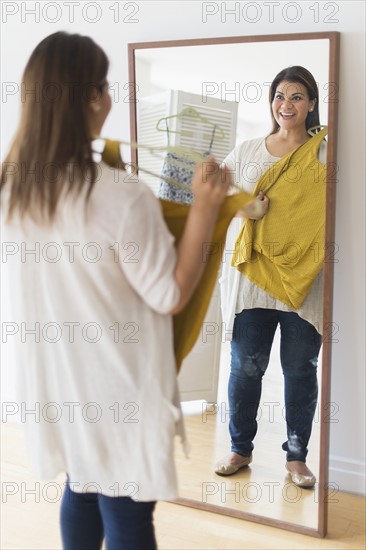 Woman holding new dress and looking at mirror.