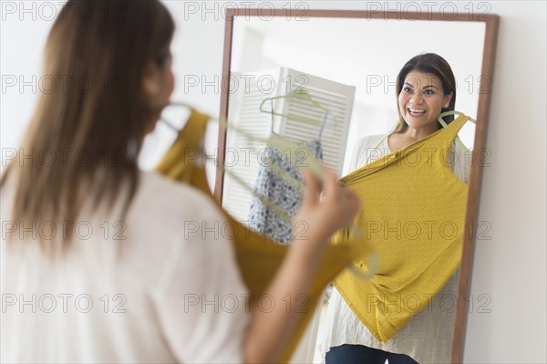 Woman holding new dress and looking at mirror.