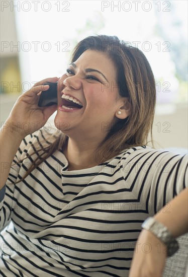 Happy woman sitting on sofa with mobile phone.