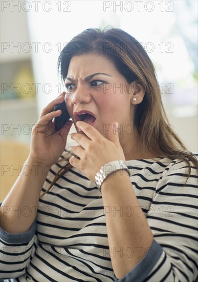 Surprised woman sitting on sofa with mobile phone.