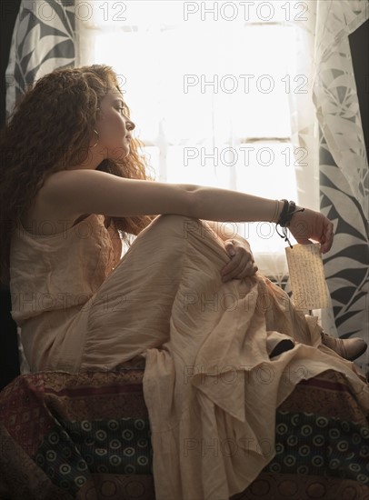 Portrait of stylish woman sitting in window sill.