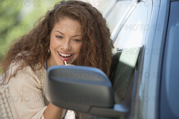 Young woman putting lipstick looking at rear mirror.