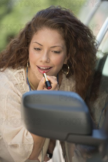 Young woman putting lipstick looking at rear mirror.