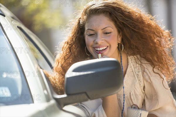 Young woman putting lipstick looking at rear mirror.