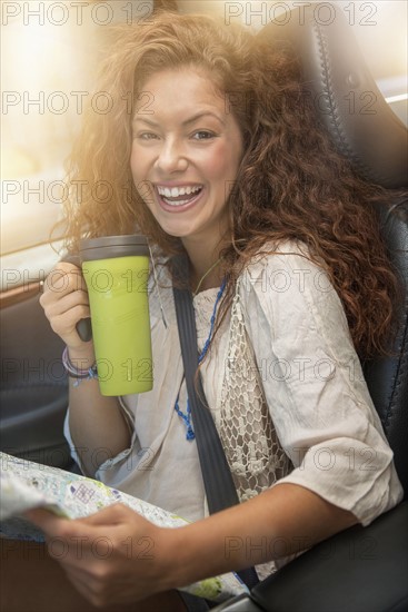 Woman sitting in car with map and disposable cup.