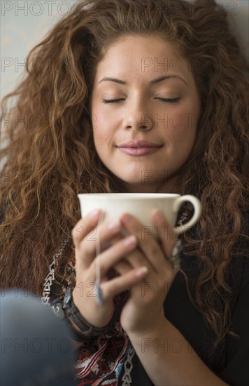 Portrait of woman sitting on bed with tea cup and closed eyes.