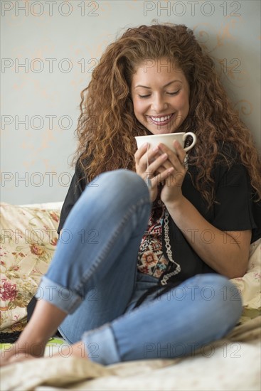 Portrait of woman sitting on bed with tea cup.