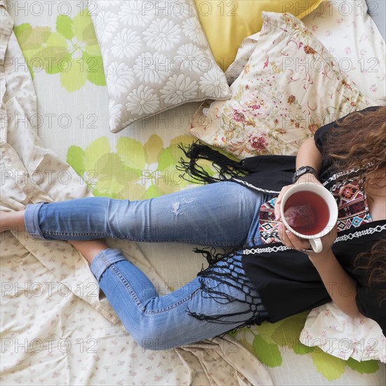 Woman lying down on bed with tea cup.