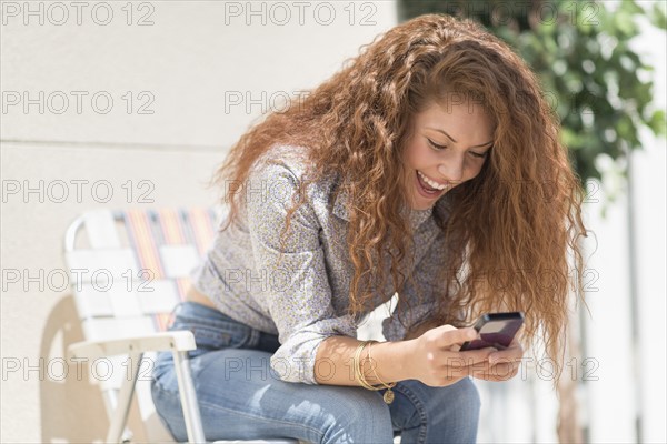 Portrait of woman sitting in deck chair outdoors with mobile phone.