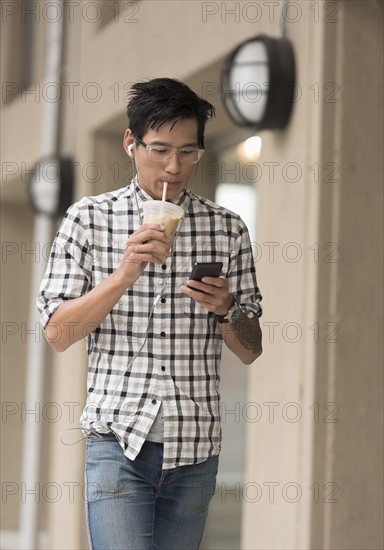 Man walking on sidewalk with iced coffee and mobile phone.