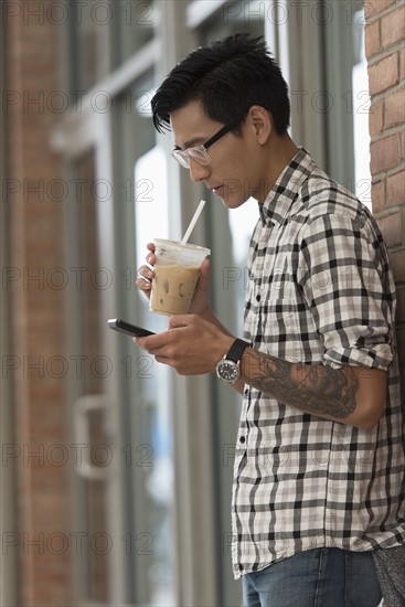 Man walking on sidewalk with iced coffee and mobile phone.