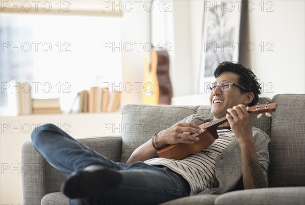 Man sitting on sofa and playing ukulele.