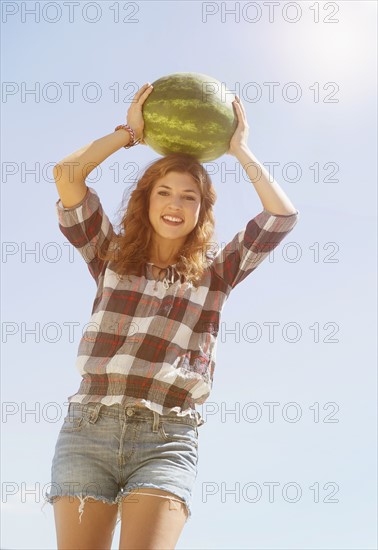 Young woman carrying on head watermelon.