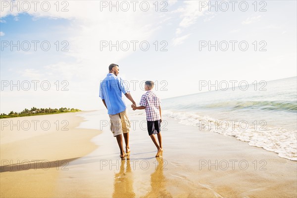 Father and son (10-11) walking on beach