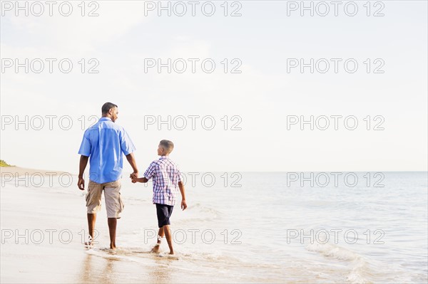 Father and son (10-11) walking on beach