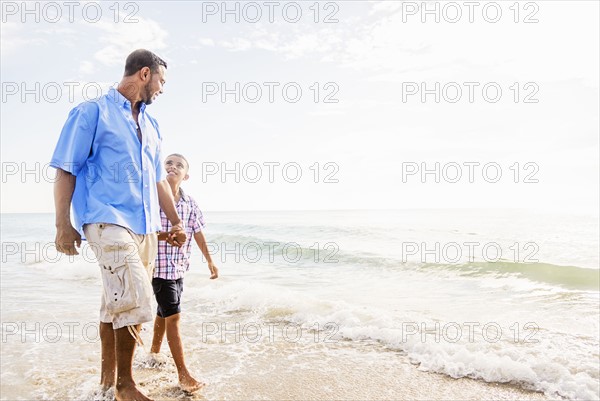 Father and son (10-11) walking on beach