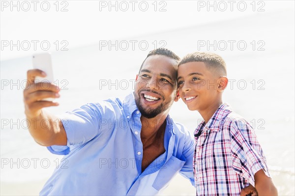Father and son (10-11) photographing self on beach