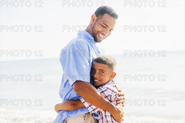 Father and son (10-11) embracing on beach
