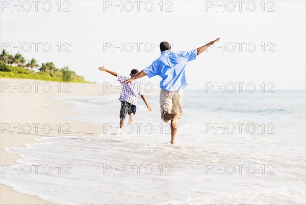 Father and son (10-11) running on beach