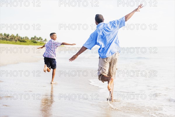 Father and son (10-11) running on beach