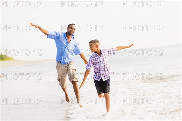 Father and son (10-11) running on beach