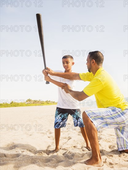 Father and son (10-11) playing baseball on beach