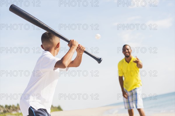 Father and son (10-11) playing baseball on beach