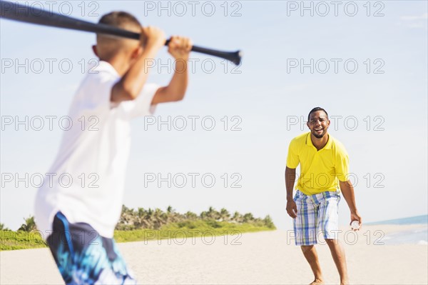 Father and son (10-11) playing baseball on beach