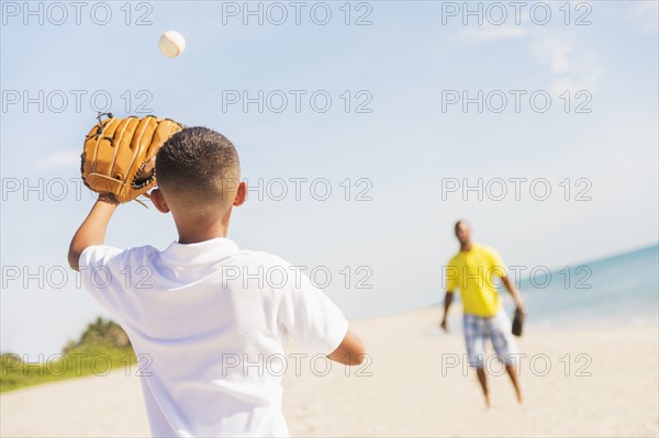 Father and son (10-11) playing baseball on beach